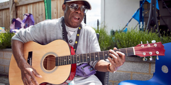 Fernando, a black man wearing sunglasses, playing an acoustic guitar.