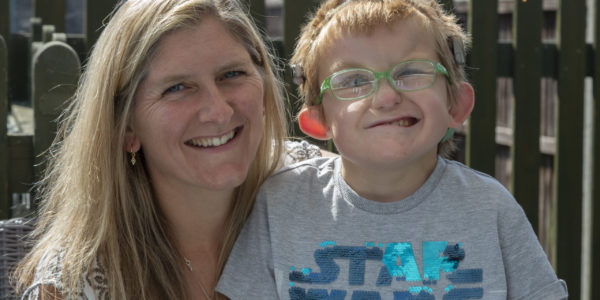 Hugo and his mum smile for the camera. His mum has long blonde hair, and Hugo has blue glasses and a Stars Wars t-shirt