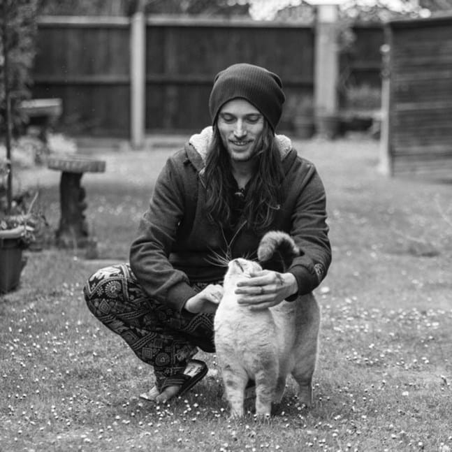 Black and white photo of man kneeling down in a garden stroking a cat