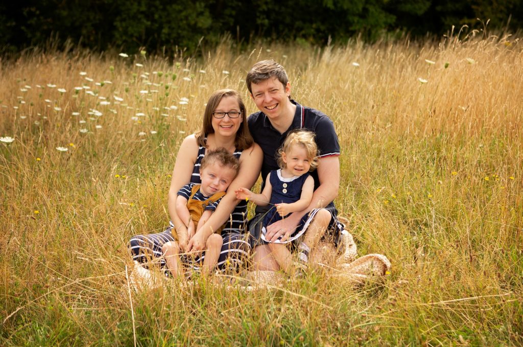 A man and a woman sitting outside in a field with their son and daughter. They're all smiling. / --

