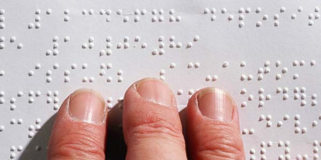 A close-up of three fingers resting on a page marked with braille