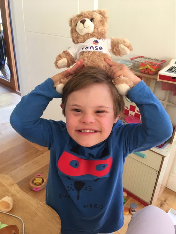 Ernie is beaming with a smile, he's holding Teddy Sense, a soft cuddly bear, on his head