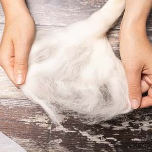 Image shows hands teasing out some of the white merino.