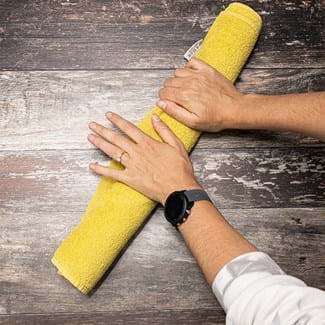 The mesh is rolled up inside a yellow towel and two hands are rolling it over a table