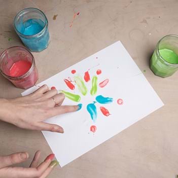 A hand is doing some finger painting using red, blue and green paints