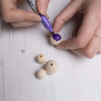 Hands colouring in small beige beads with a purple felt-tip pen