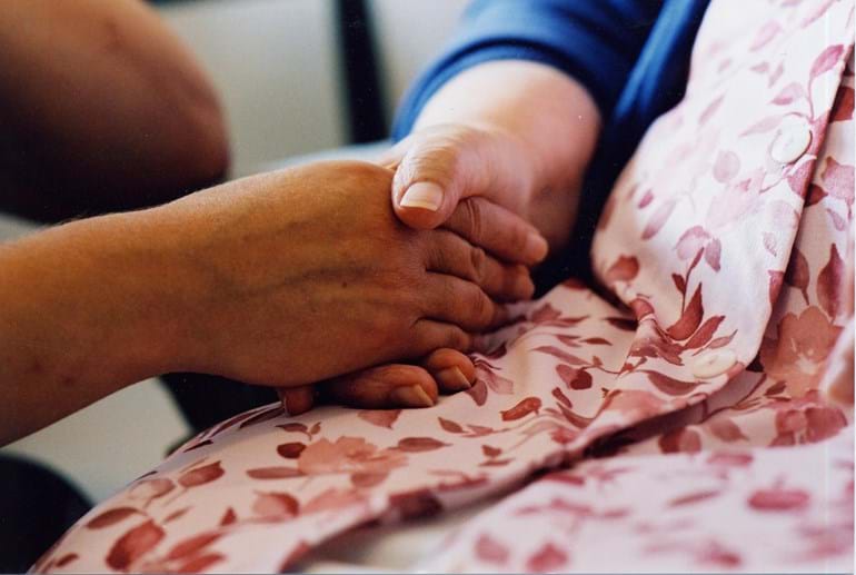 A close-up on two holding hands, resting in a woman's lap who's wearing a pink floral dress