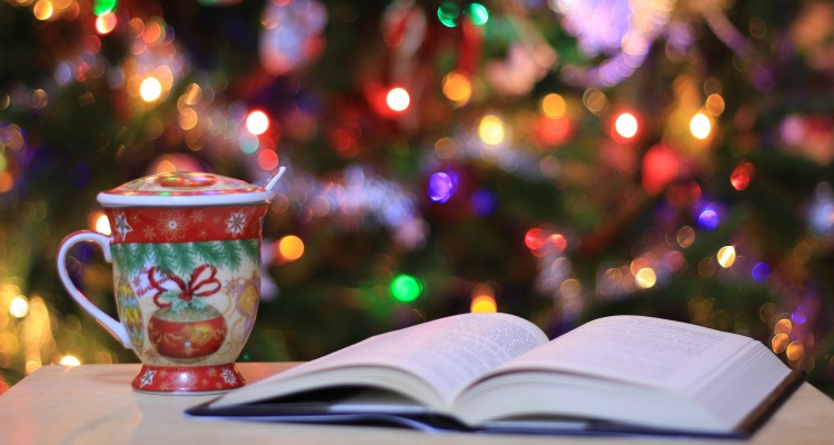 A Christmassy scene with a mug and an open book with a Christmas tree in the background