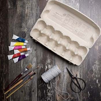 An egg box, string, paints, a pair of scissors and brushes on a wooden background