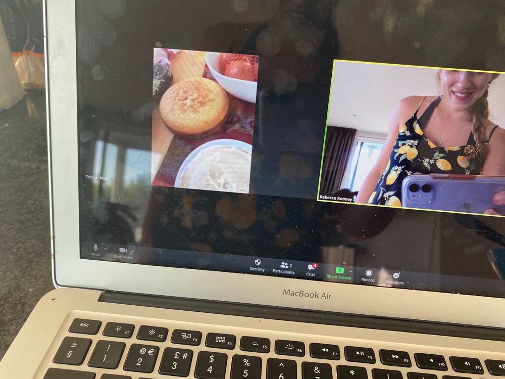 A picture of a screen. On the screen there are two squares. It's a video call. In one square, we can see a cake. In the other, a woman is taking a photo with her phone of the screen.