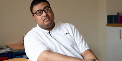 A young man in a white poloshirt leaning on a table