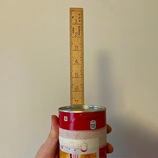 A hand holds the crisp tube upside down and a wooden ruler is taped to the tube with half of it extended out.
