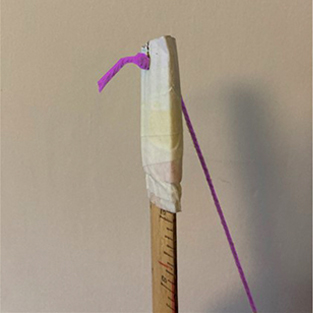 Ruler with string threaded through the notch made in the cardboard with a knot tied at the end.
