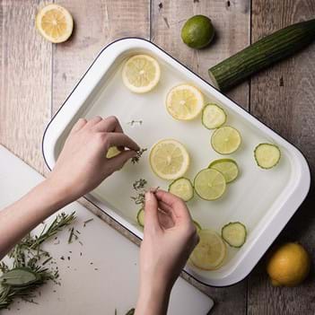 A hand is placing slices of lemons and limes into a dish of water