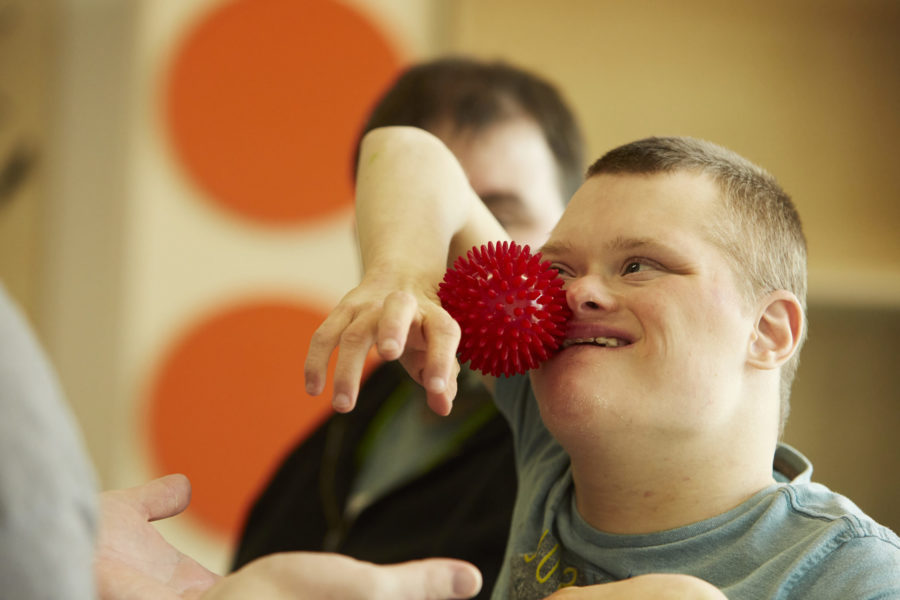 Young man taking part in dance class at Sense TouchBase Pears. He is holding a spiky, sensory ball between his arm and his cheek.