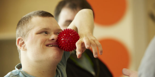 A young man smiling and playing with a red ball.