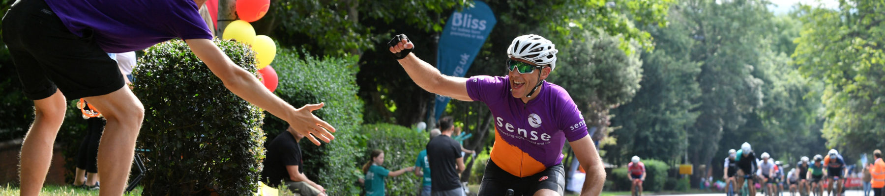 A male cyclist in a Sense jersey high fiving spectators
