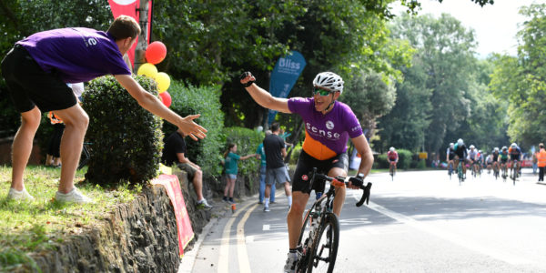 A male cyclist in a Sense jersey high fiving spectators