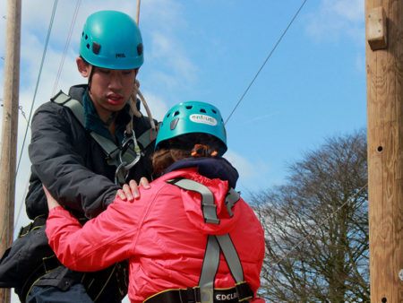 A young man is being held by an instructor before he does a zip line - they're both wearing safety gear