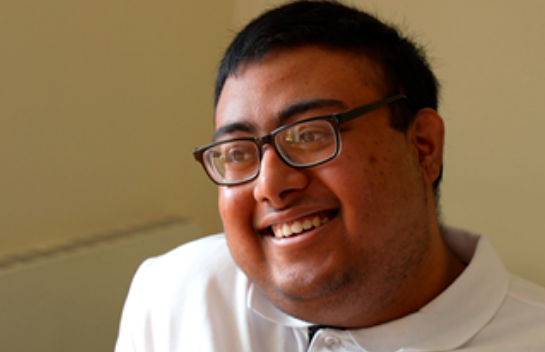 Saihan, a young man with glasses and short black hair, smiling
