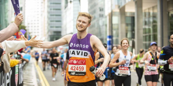 A man wearing a Sense vest reaches out to supporters while running the London marathon.