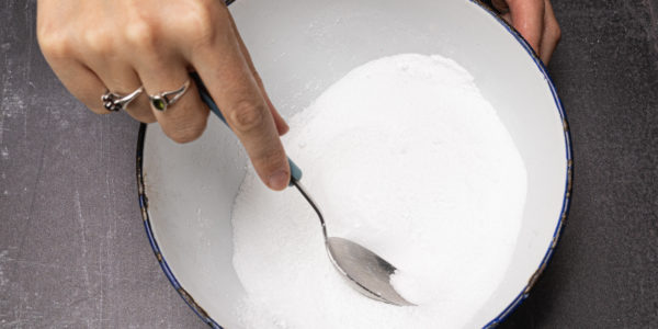 A hand mixes the citric acid and bicarbonate of soda in a bowl.