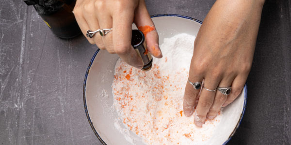 Hands are in the bowl with the orange mixture rubbing it together