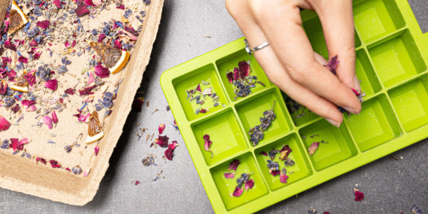 A hand sprinkling dried flowers into the silicone moulds