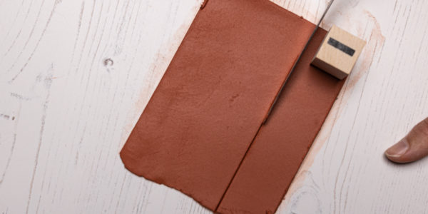 Image shows the hand cutting a strip of clay, using a letter stamp to mark out the required width for the slice.
