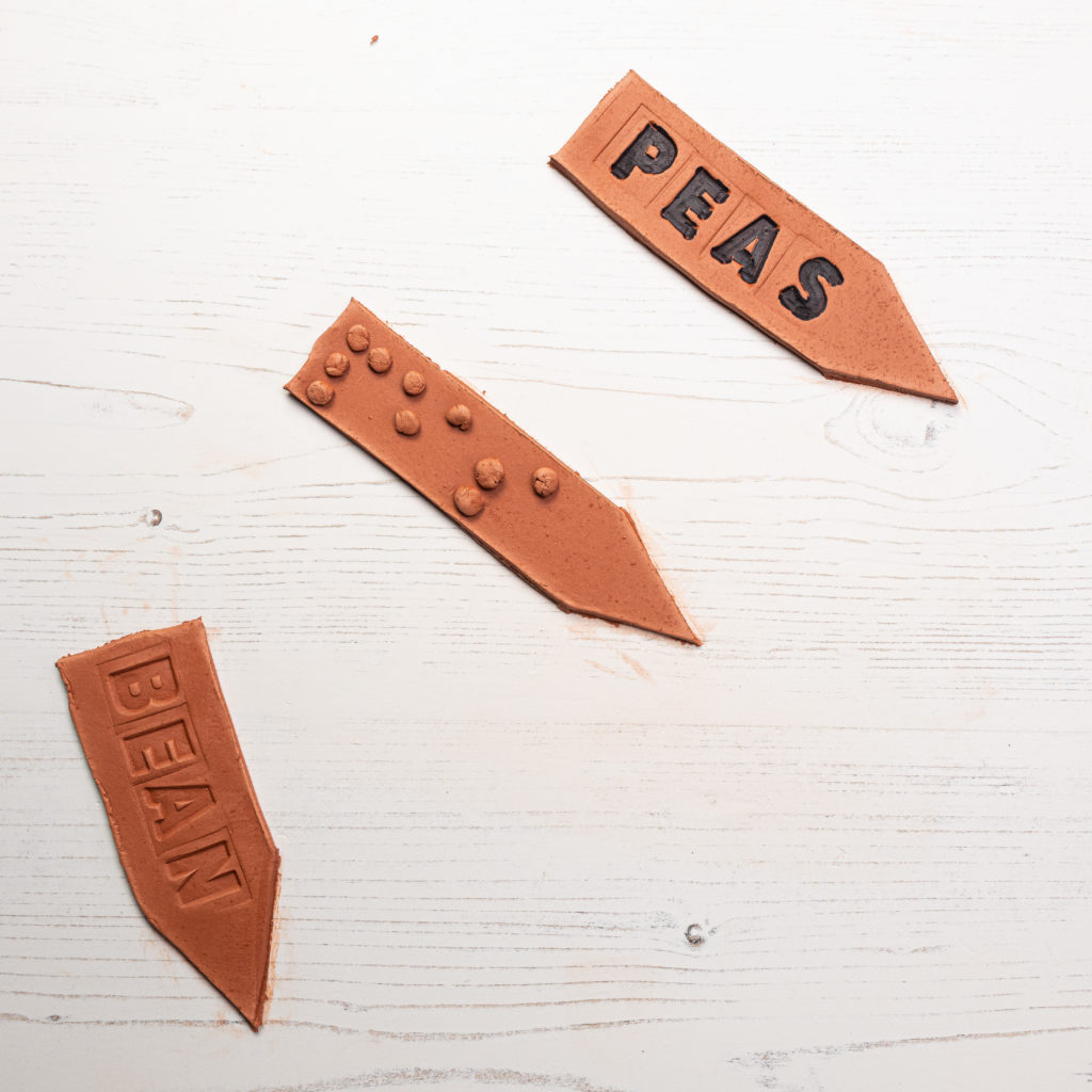 Image shows 3 finished plant markers, top one has black bold letters, the second braille and the third stamped letters.