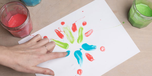 A hand is doing some finger painting using red, blue and green paints