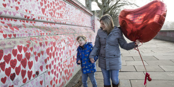 A woman holding a heart-shaped balloon and a young boy at the National Covid Memorial Wall in London.