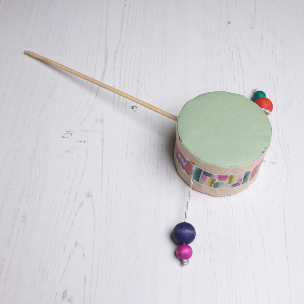 A hand drum with colourful beads, on a long wooden stick