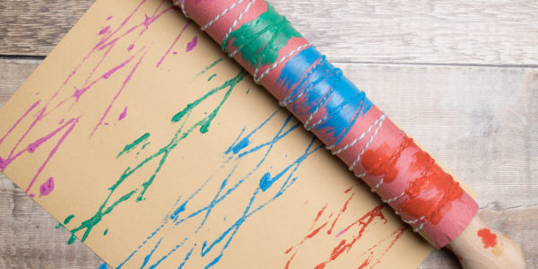 Pour paint onto your palette, and roll the rolling pin into the paint. Then, roll the rolling pin across the paper, and explore layering different colours, textures and shapes.