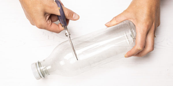 Image shows hand cutting bottle.
