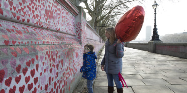A boy and a woman look at red hearts painted on a wall