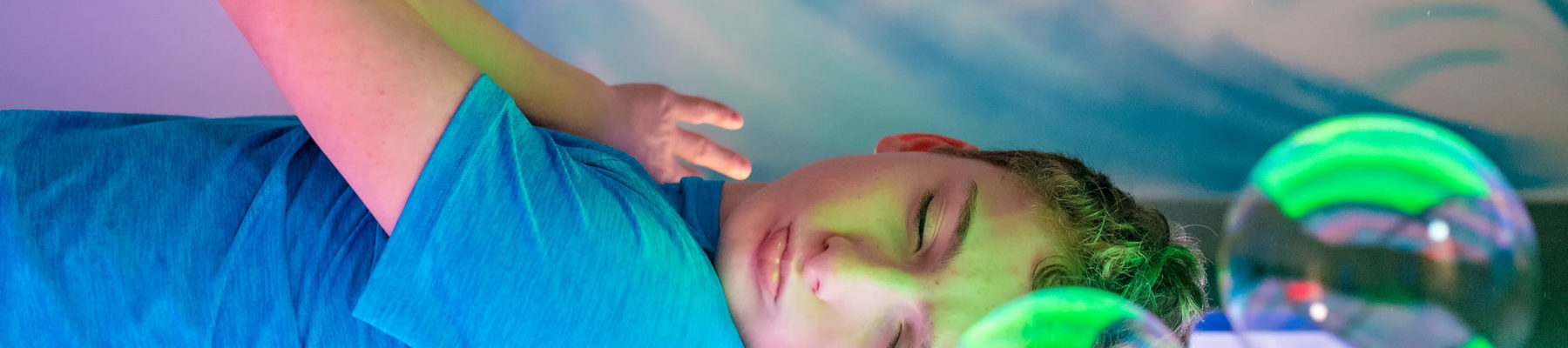 Boy relaxing in multi-sensory room with bubbles.