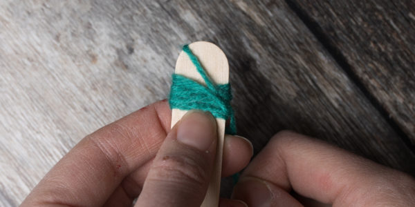 Wrapping green yarn around a lollypop stick