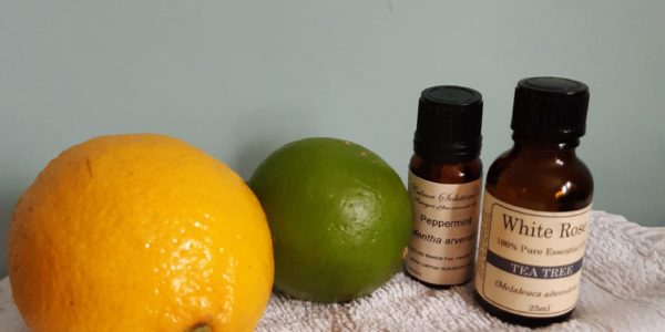 An orange, a lime, and essential oils on a white towel against a light blue background