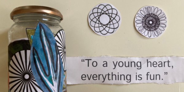 A finished jar on the left covered in black and white shapes and a blue leaf on the front. A piece of paper on the table also reads “To a young heart, everything is fun”