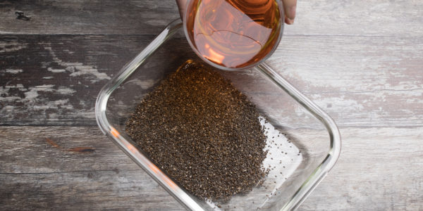 Chia seeds in a tub being covered with a pink-ish water