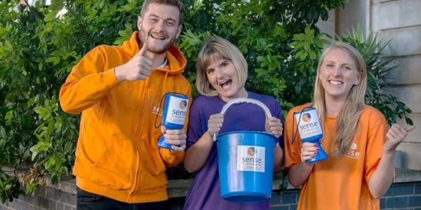 Three people in a row wearing Sense colours, holding fundraising buckets and smiling