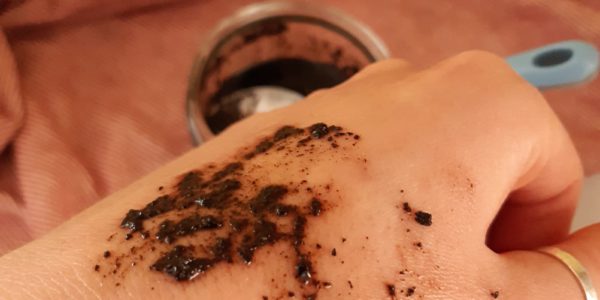 The back of someone's hand, with a smear of the dark brown exfoliant on it