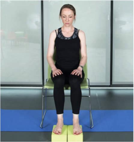 a woman sitting on a chair with her hands on her thighs and her feet on blocks