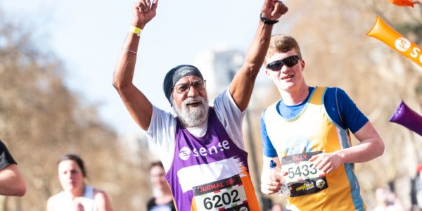 A older man in a Sense running vest holds his hands as he runs in a marathon