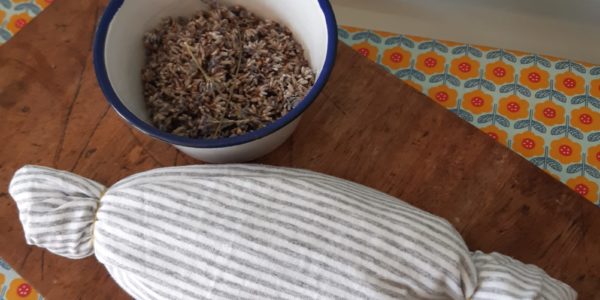 A white, stripey eye pillow secured at both ends with elastic, and a bowl of lavender