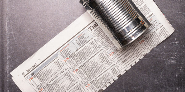 Image shows a strip of newspaper, with a can placed on the right side of it, the can pokes out above the newspaper by 3cm