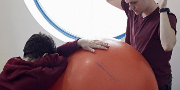 Two boys playing with a very big orange ball