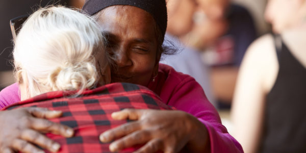 Raji, an Asian woman, hugs another person whose back is to the camera.