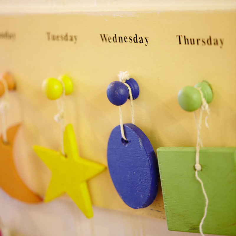 A hanging yellow star, blue circle and green square on pegs above which say the days of the week